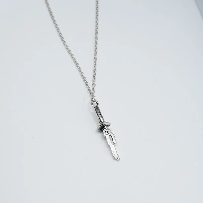 The necklace in the image features a pendant designed like a sword. Here are some observations about the necklace:
Pendant:
Shape: The pendant resembles a sword with a curved blade and a distinctive hilt.
Material: The pendant appears to be made of silver, given its shiny appearance.
Details: There are intricate details on the hilt, including a circular design and what might be a letter or symbol