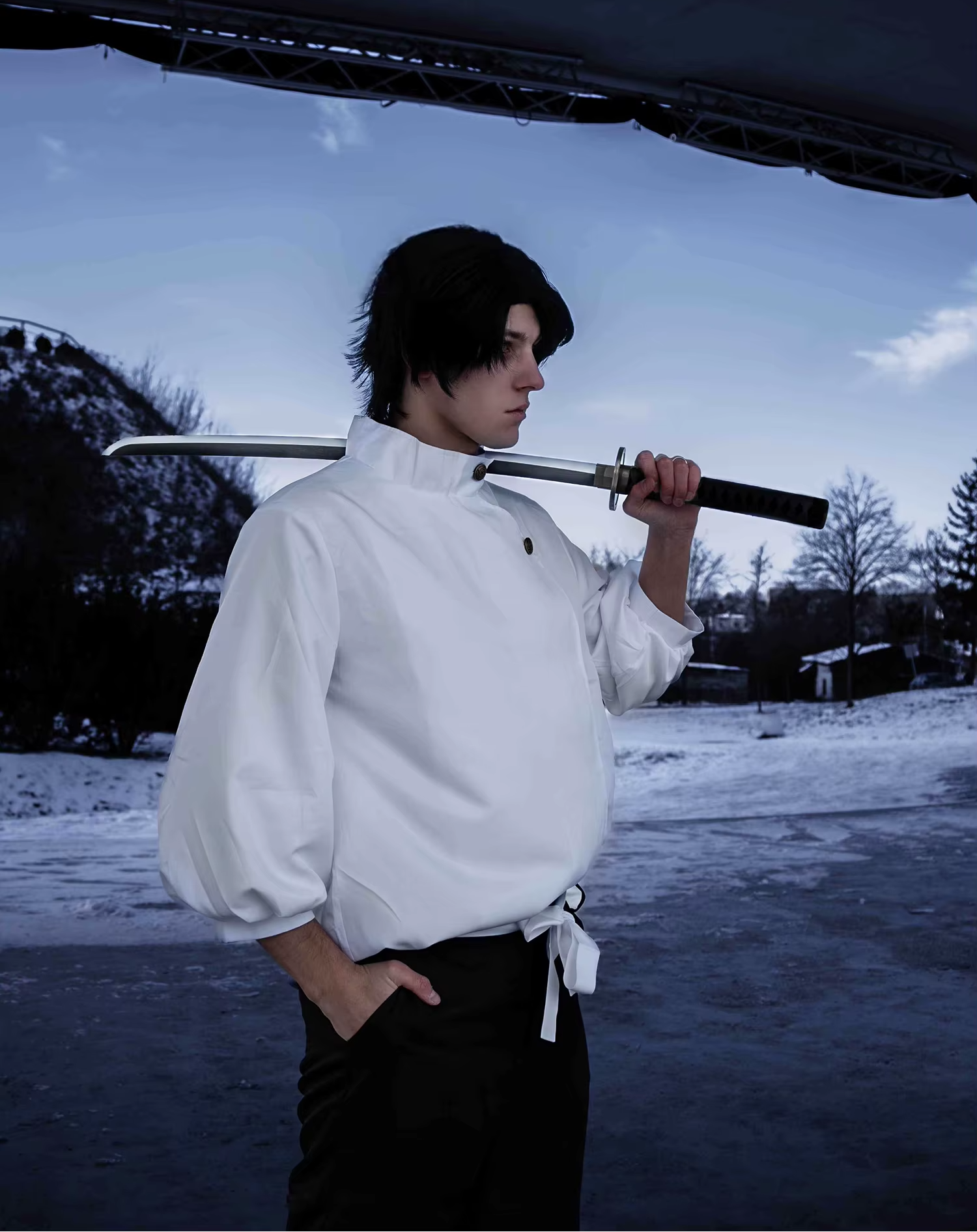 Person in a white shirt holding a sword in a snowy landscape with trees and a building in the background.