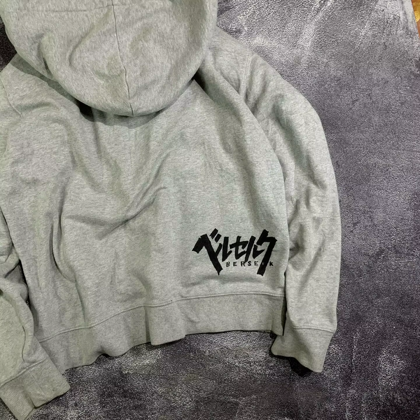 Close-up of the black Japanese Katakana Berserk logo printed on the back hem of a heather grey hoodie
