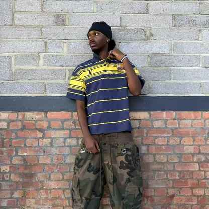 Model wearing the Navy and Yellow striped oversized terrace polo with the FCUL crest, paired with camo cargos and a black beanie.