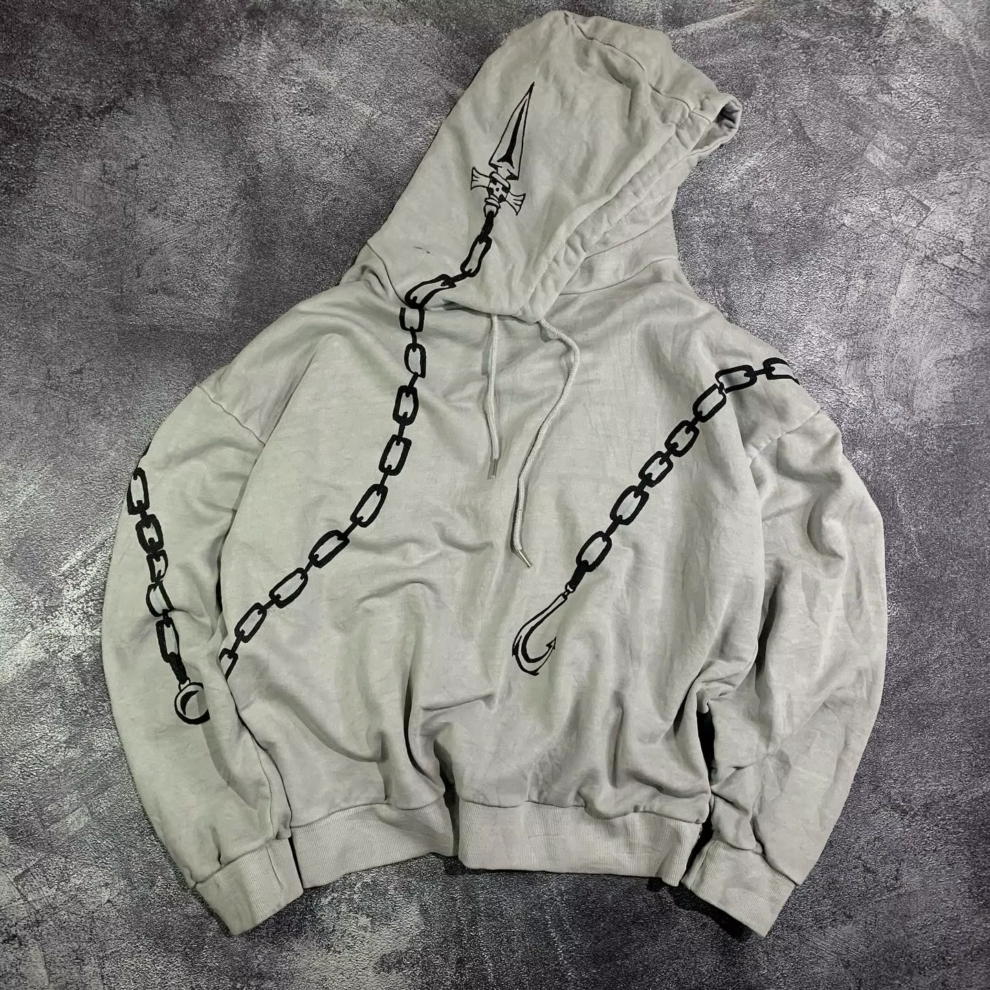 Front view of an oversized grey anime hoodie featuring wrap-around chain graphics and a judgment blade printed on the hood.