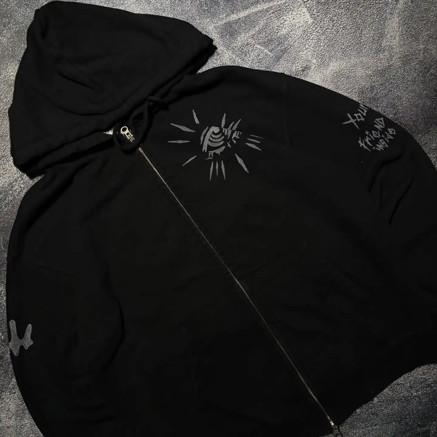 Close-up of custom evil eye and sleeve text embroidery on a black heavyweight zip-up hoodie.