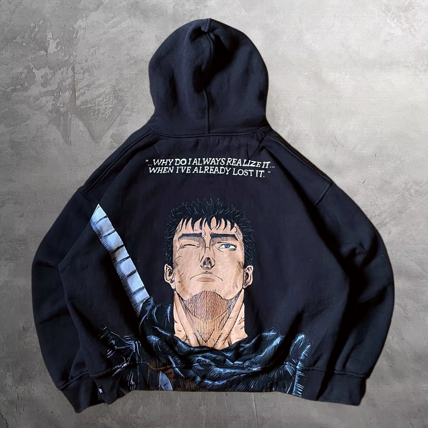 Flat lay of the back of a black streetwear hoodie featuring a massive Guts manga portrait and quote by SkaiiyPrints.