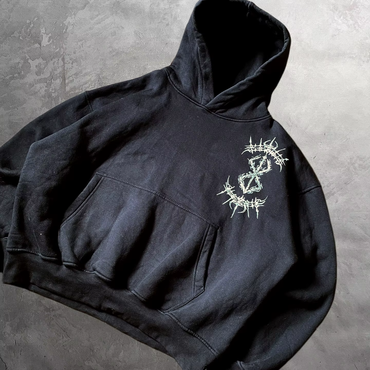 Angled front view of a black drop-shoulder hoodie featuring a stylized cyber-sigilism Brand of Sacrifice chest print.