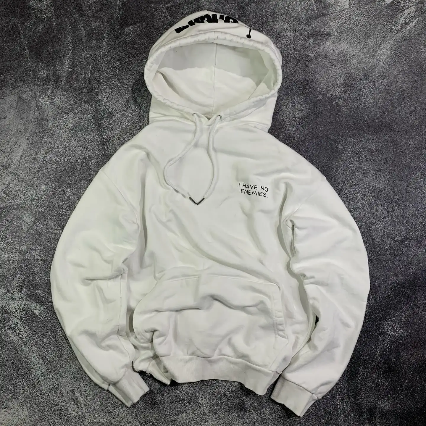 Front view of a white oversized heavyweight pullover hoodie featuring minimalist 'I have no enemies' chest typography by SkaiiyPrints