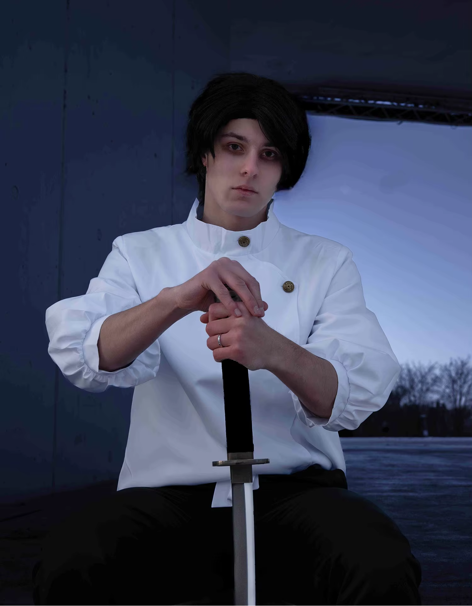 Person in a white shirt holding a sword against a dark background